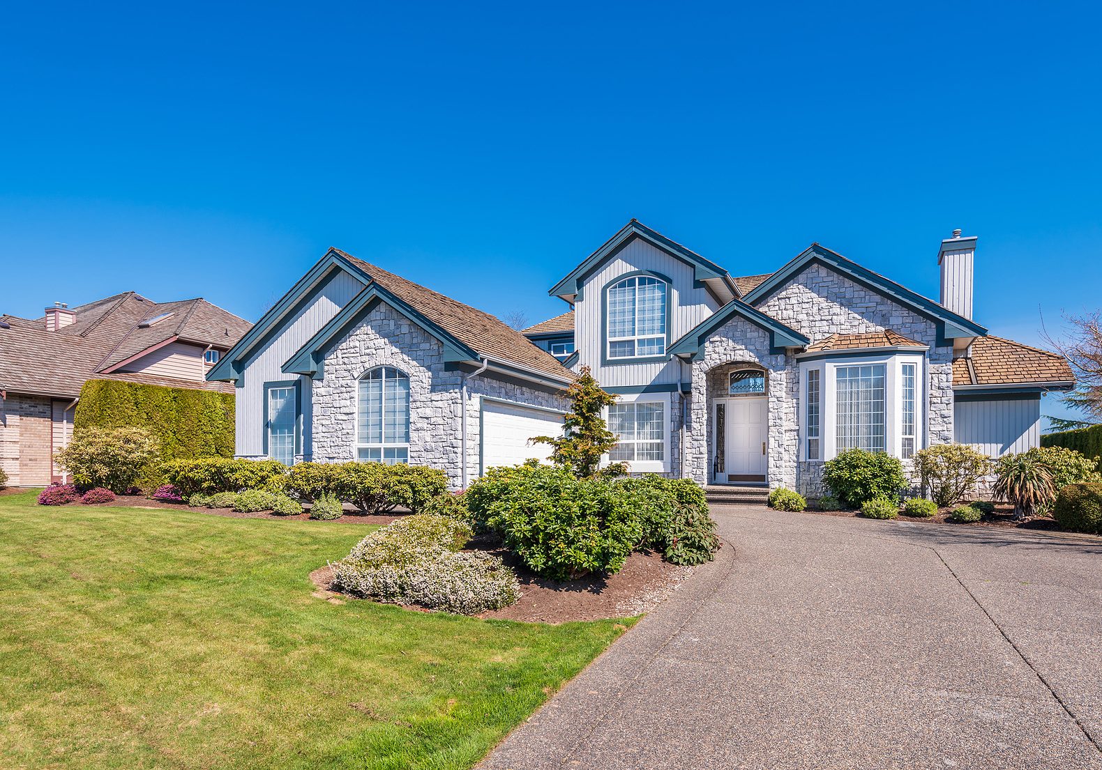 Beautiful exterior of newly built luxury home. Yard with green grass and walkway lead to ornately designed covered porch and front entrance.