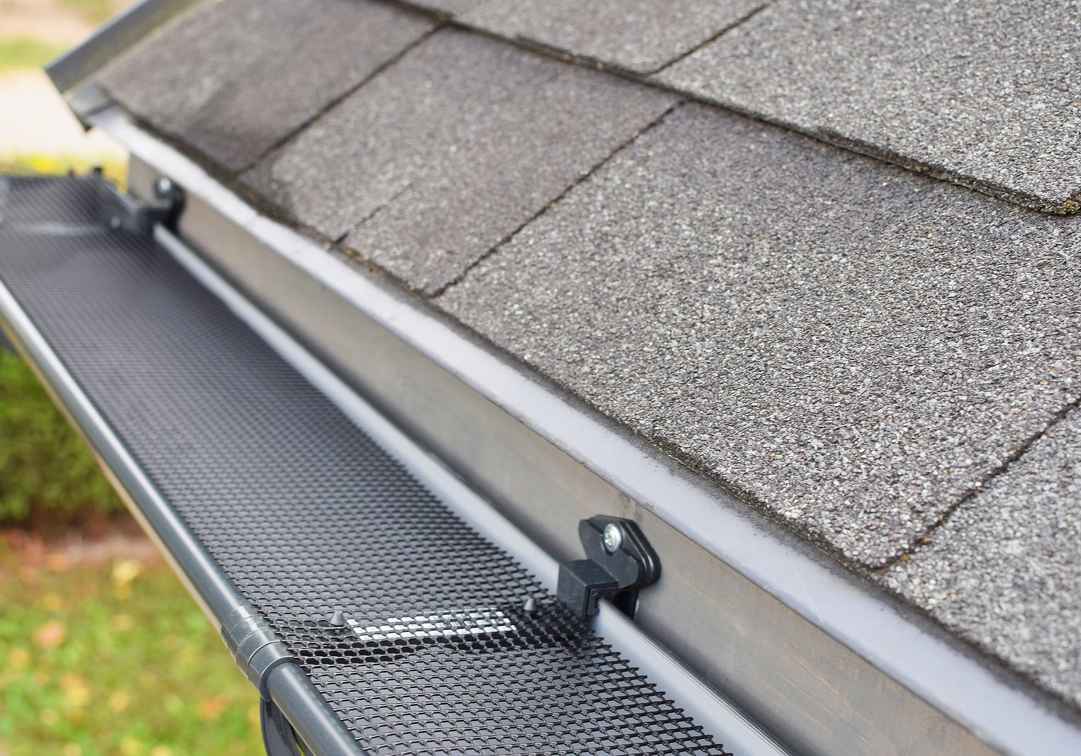 Plastic guard over new dark grey plastic rain gutter on asphalt shingles roof at shallow depth of field.