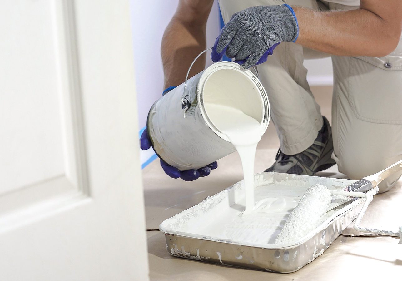 Professional Interior Construction Worker Pouring White Color Pa Close up of painter hands with gloves painting the wall edge with brush. Hand painting above molding, baseboard.